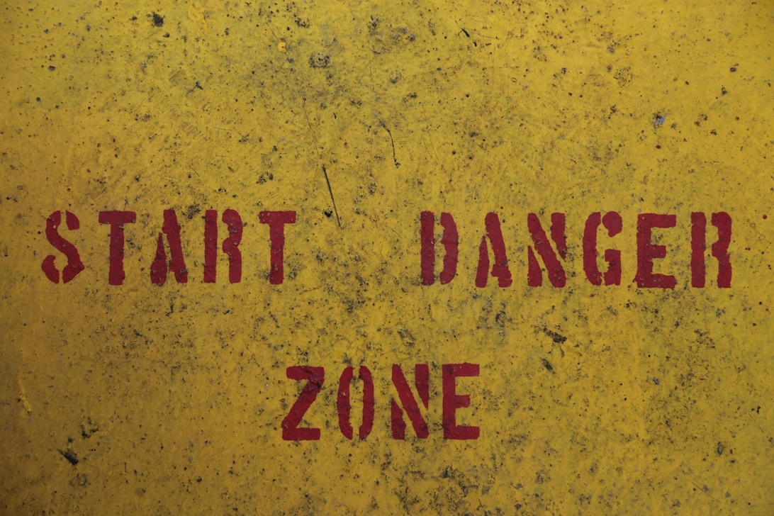 A weathered yellow industrial surface with bold red stenciled text reading 'START DANGER ZONE', featuring distressed textures and industrial warning aesthetics.