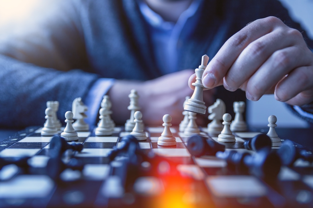 A businessman in formal attire making a strategic chess move on a wooden chessboard, with professional lighting and blue tones creating a corporate atmosphere.