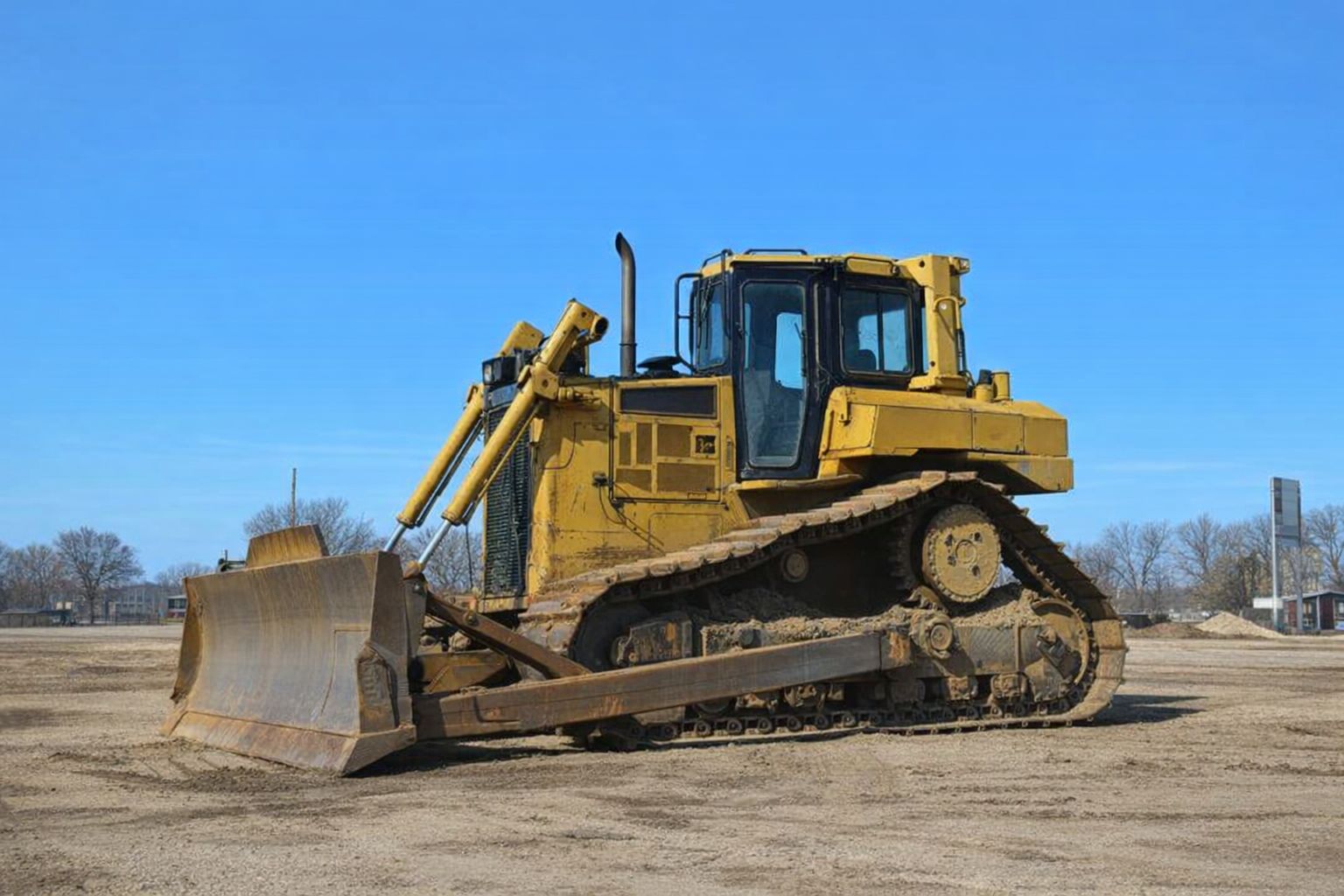 En stor gul schaktmaskin på en öppen byggarbetsplats under en blå himmel.